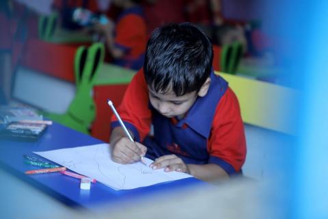 A cute schoolboy is drawing on a white paper