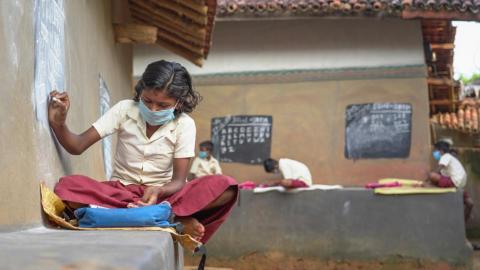 A girl student writing on a blackboard built in a mud wall during covid-19